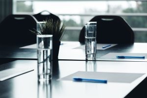 Close up of dark conference table water glasses pens, paper sheets